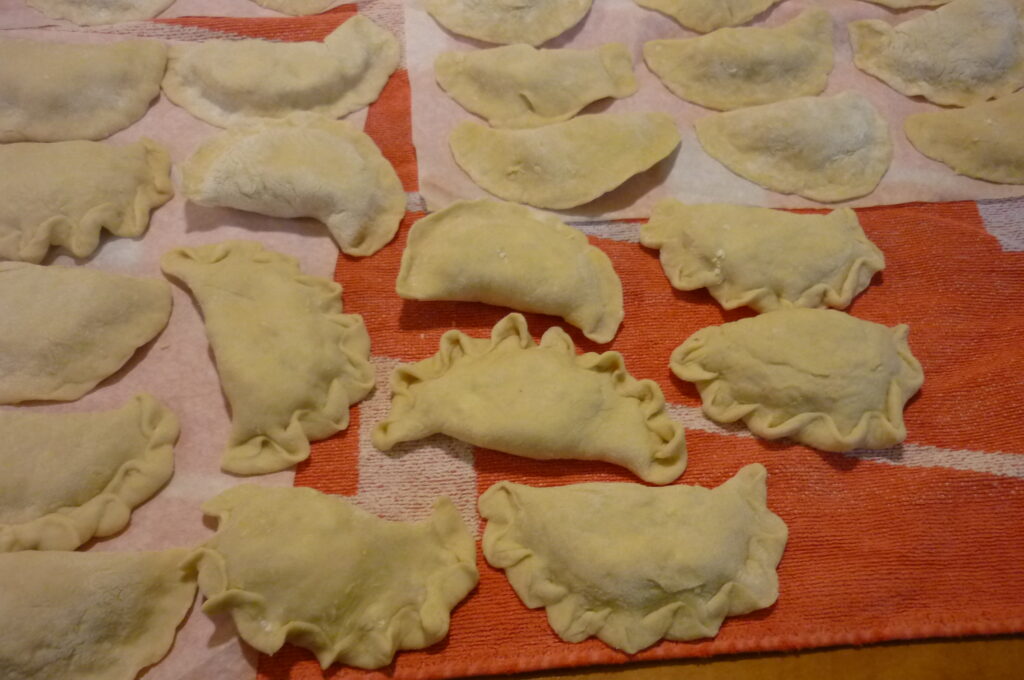 Świeżo zrobione pierogi, jeszcze przed ugotowaniem. Ułożone są na dużym, czerwonym ręczniku wyłożonym papierem śniadaniowym